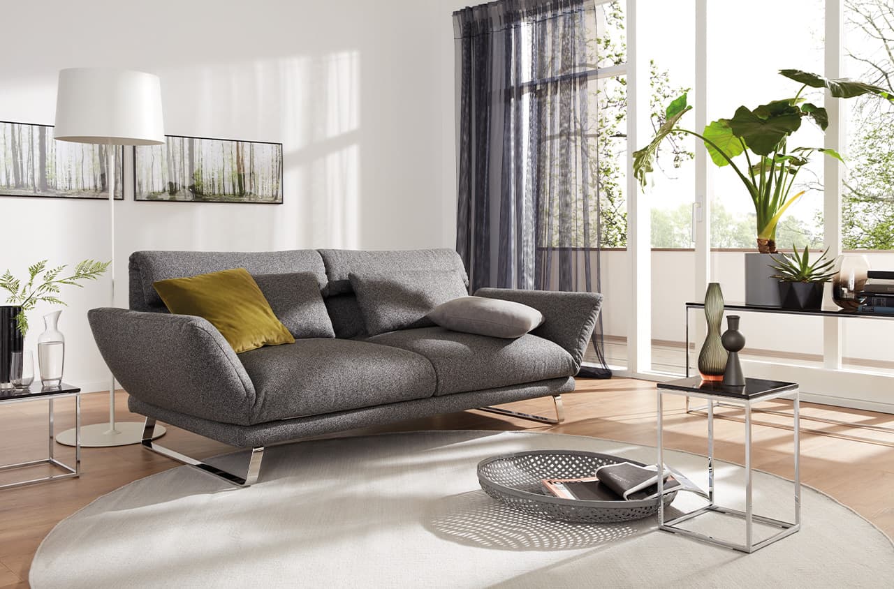Graues Sofa mit breiter Sitzfläche, weichen Polstern, leicht geneigten Armlehnen in heller, modern eingerichteter Wohnumgebung.